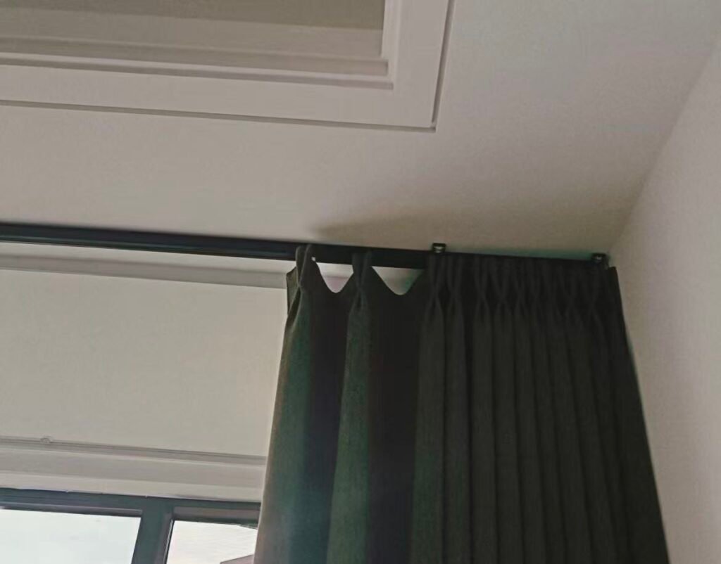A stylish, modern hotel room with large windows framed by sleek black curtain tracks holding neutral-colored curtains.