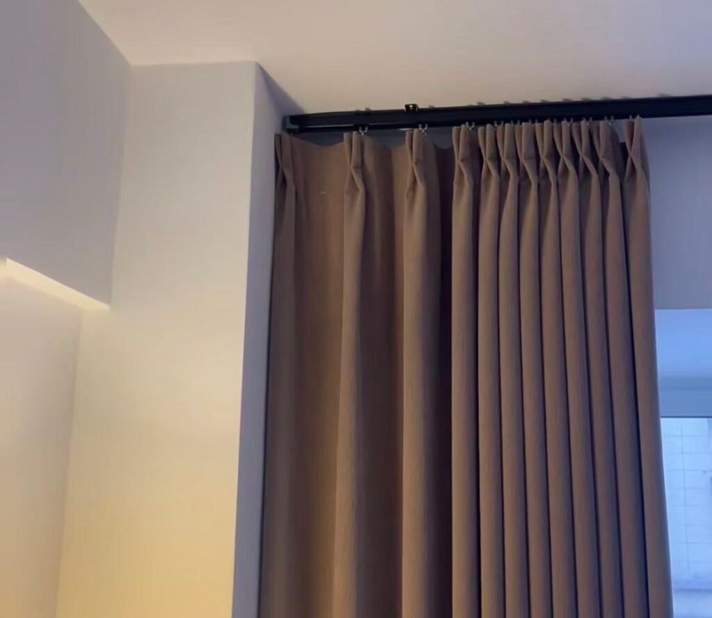 A hotel room with a black curtain track mounted close to the ceiling, making the ceiling appear higher.