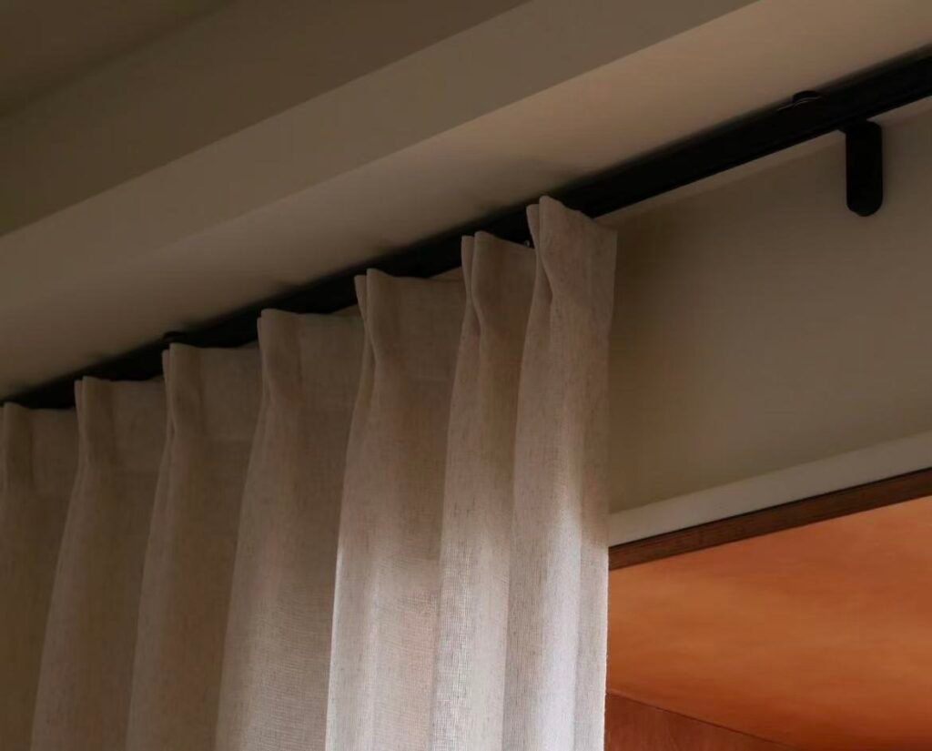 A mood board showing a black curtain track with fabric swatches of white, gray, deep green, and velvet blue.