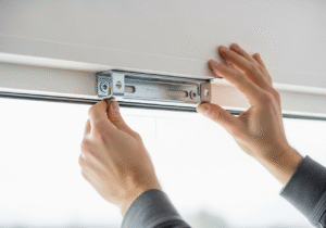 A close-up image of hands installing a center support bracket on a wall to prevent a curtain rod from sagging.